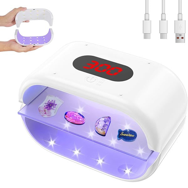 White UV nail lamp with a digital LED curing display on top, showing purple interior lighting and several sample gemstones inside. A small inset shows a pair of hands holding the lamp open, and another inset shows two USB charging cables on a white background.