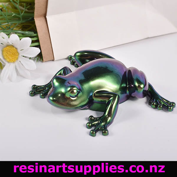 Iridescent frog sculpture on a white surface with flowers in the background