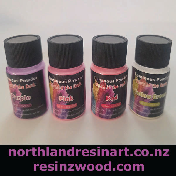 Four bottles of luminous powder with black lids on a white background, featuring purple, pink, red, and yellow labels.