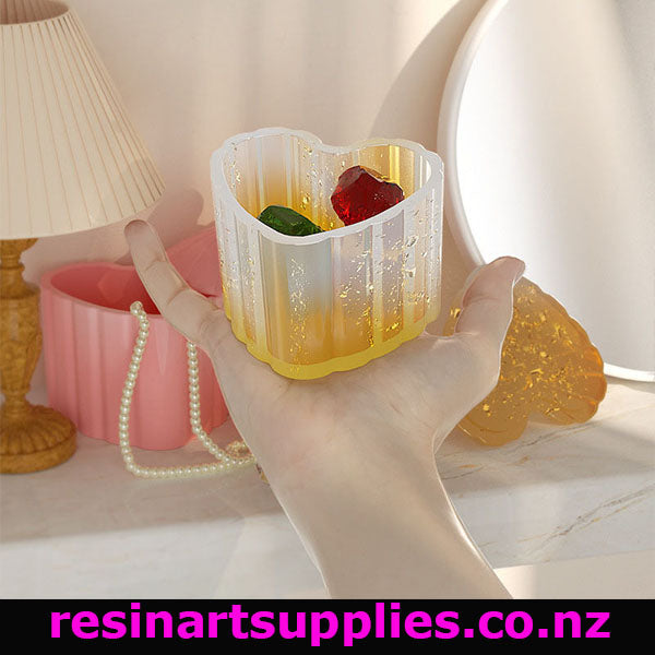 Hand holding a resin mold with gummy bear shapes on a decorative surface.