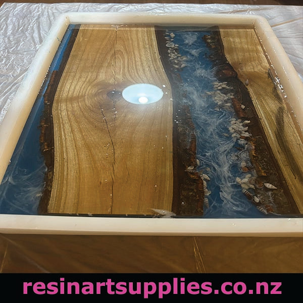 Wooden surface with blue resin and white stones, branded 'resinartsupplies.co.nz'.