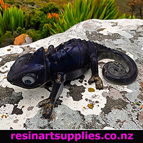 Chameleon colour paste resin. Chameleon resin sculpture on a textured stone surface with greenery in the background