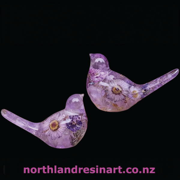 Two purple resin birds with floral designs on a black background, featuring the brand 'northlandresinart.co.nz'.