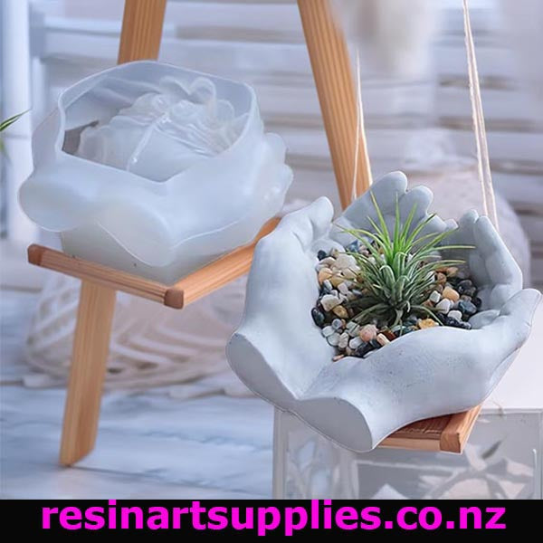White resin mold shaped like a hand holding a plant on a wooden stand with 'resinartsupplies.co.nz' branding.