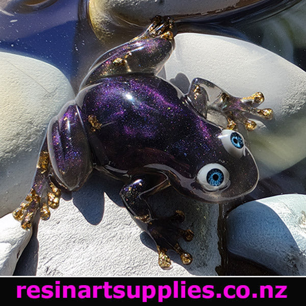 Glass frog figurine on stones with 'resinartsupplies.co.nz' text